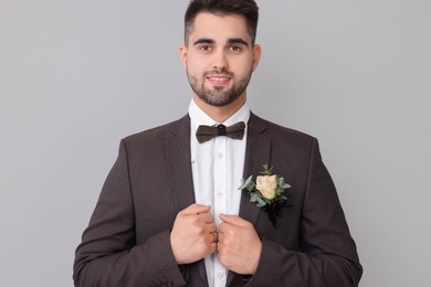 Photo of Handsome young groom with boutonniere on light grey background. Wedding accessory