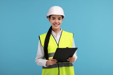 Photo of Engineer in hard hat holding clipboard on light blue background