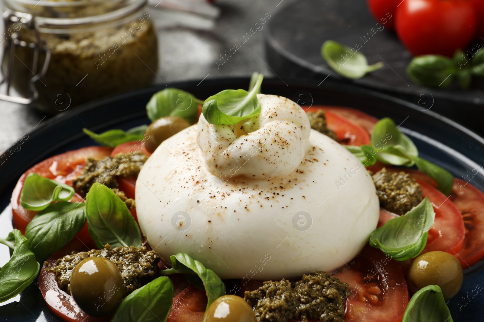 Photo of Delicious burrata salad with tomatoes, olives, basil and pesto on plate, closeup