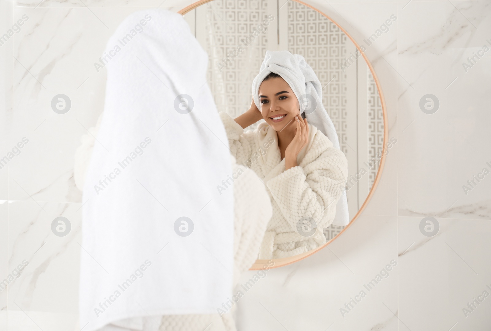 Photo of Young woman with hair wrapped in towel near mirror indoors