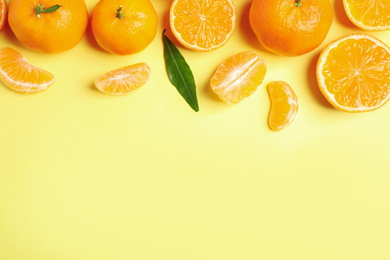 Photo of Flat lay composition with fresh ripe tangerines and leaves on light yellow background, space for text. Citrus fruit