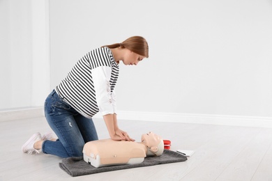 Photo of Woman practicing first aid on mannequin indoors