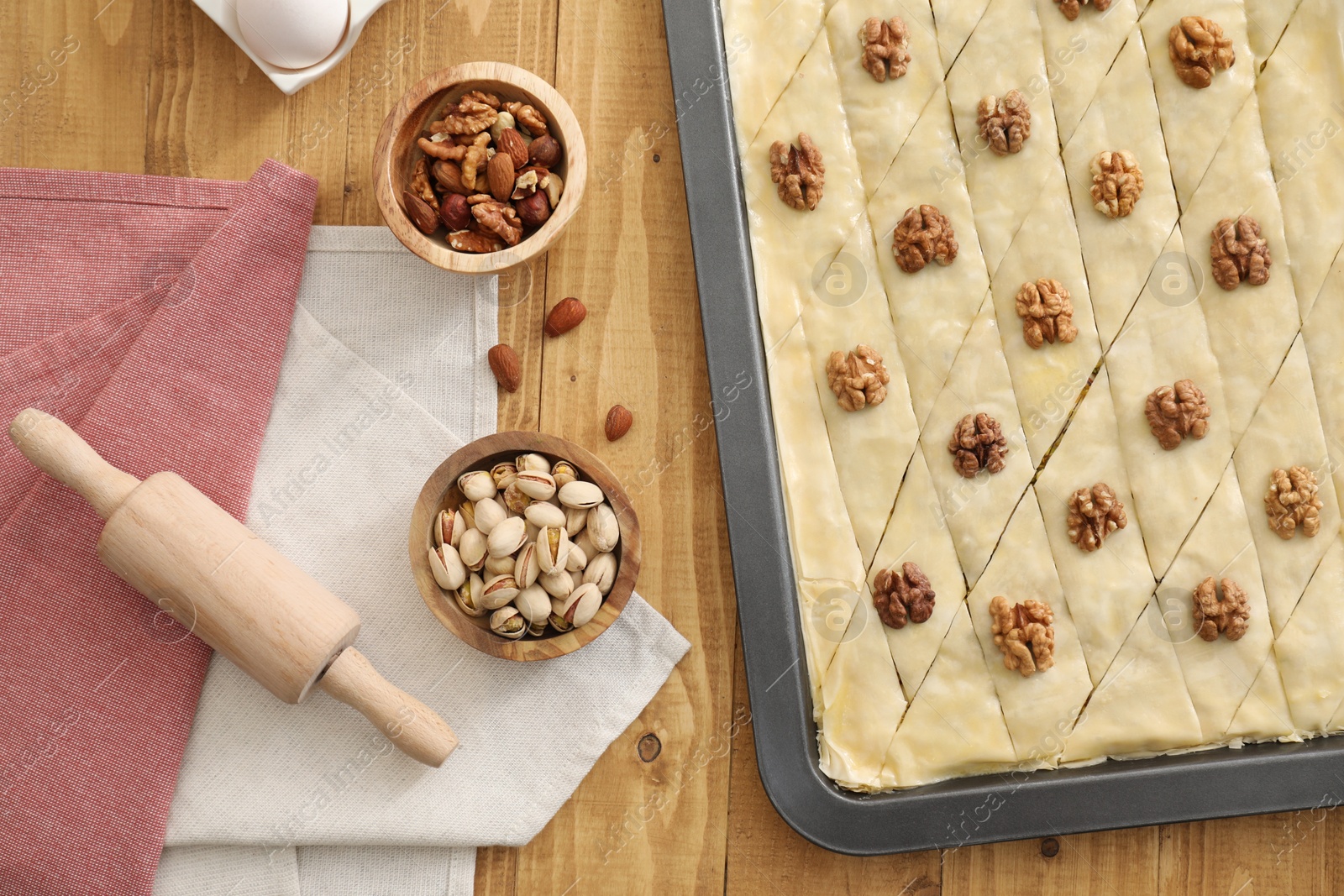Photo of Making delicious baklava. Baking pan with dough and ingredients on wooden table, flat lay