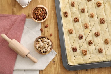 Making delicious baklava. Baking pan with dough and ingredients on wooden table, flat lay