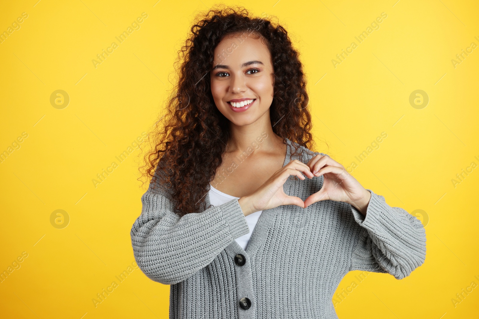 Photo of Happy young African-American woman making heart with hands on yellow background