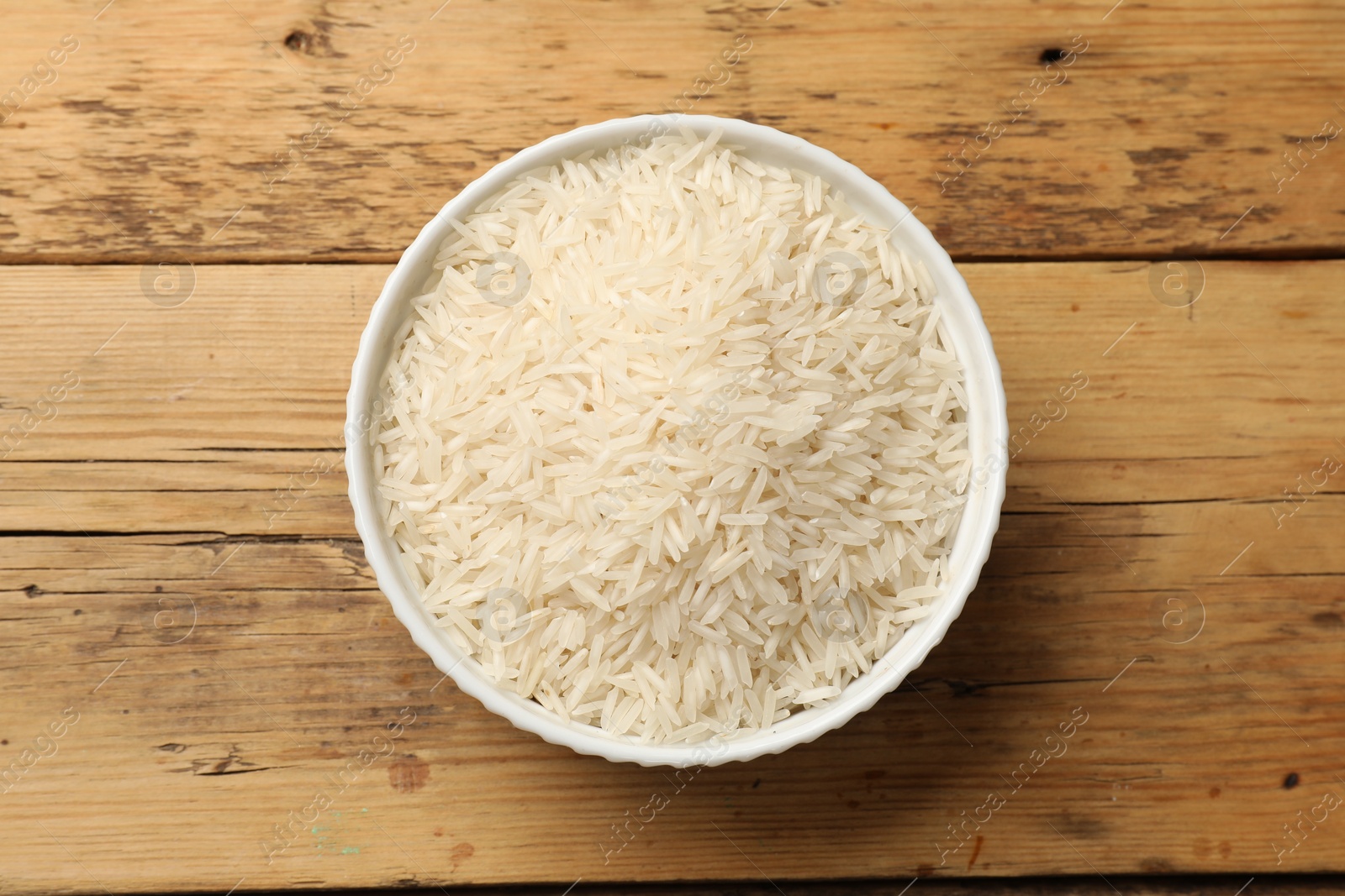 Photo of Raw basmati rice in bowl on wooden table, top view