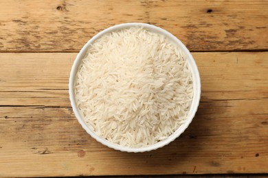Photo of Raw basmati rice in bowl on wooden table, top view