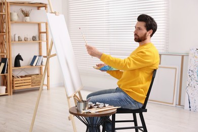 Photo of Man painting in studio. Using easel to hold canvas