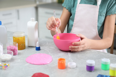 Little girl mixing ingredients with silicone spatula at table in kitchen, closeup. DIY slime toy