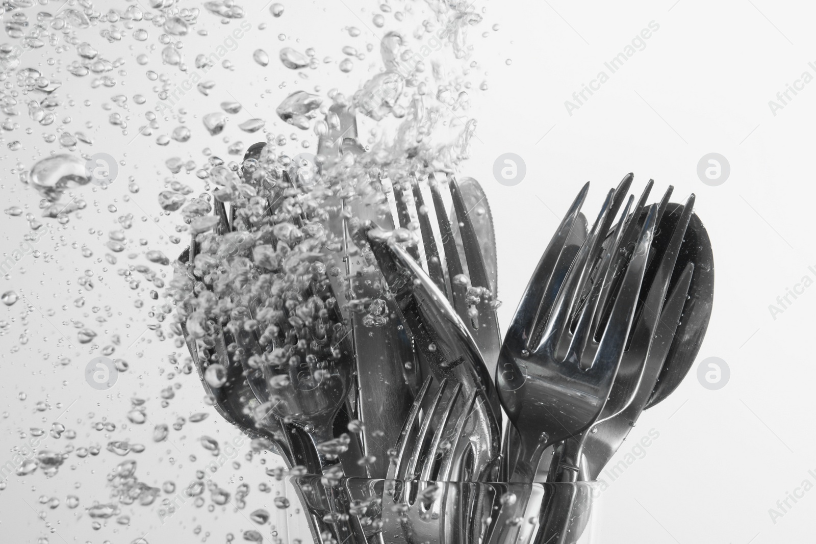 Photo of Washing silver cutlery in water on white background