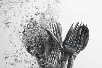 Photo of Washing silver cutlery in water on white background