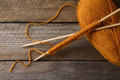 Photo of Soft orange yarn, knitting and needles on wooden table, above view