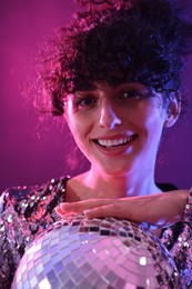 Photo of Beautiful young woman with disco ball posing on color background in neon lights, closeup