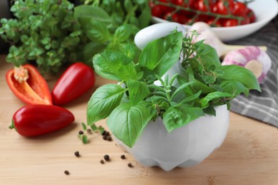 Photo of Mortar with different fresh herbs near pepper and garlic on wooden table, closeup