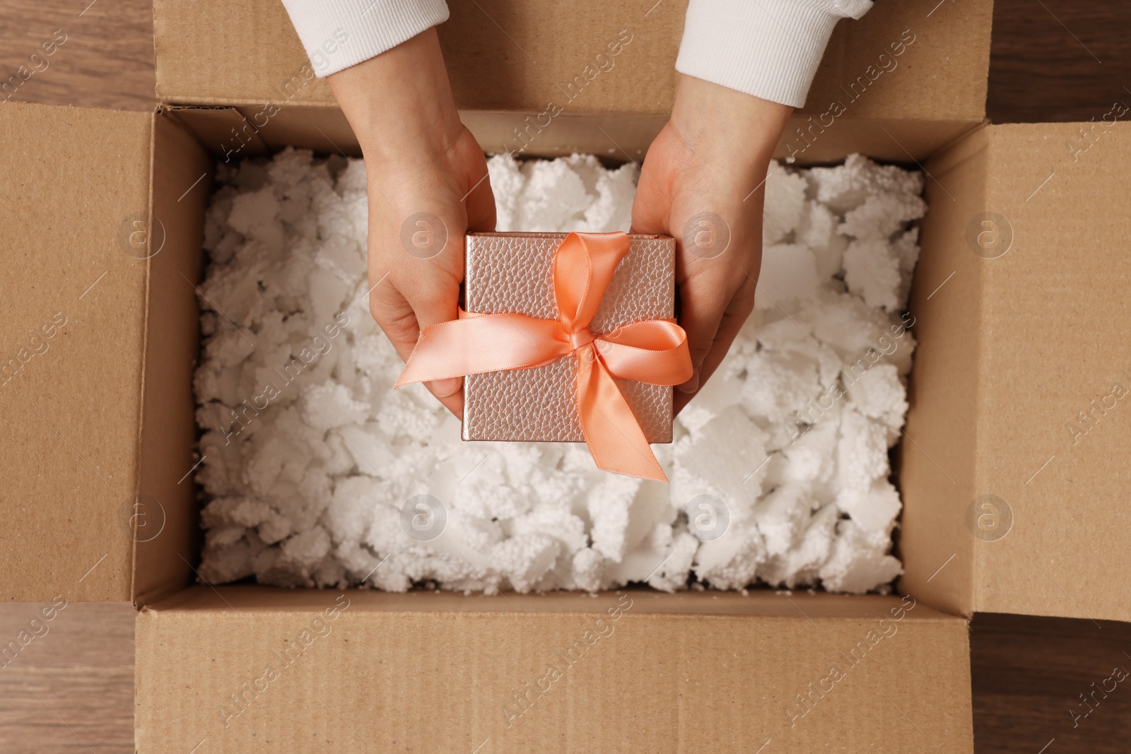 Photo of Woman putting Christmas gift box into parcel at wooden table, top view. Sending present by mail