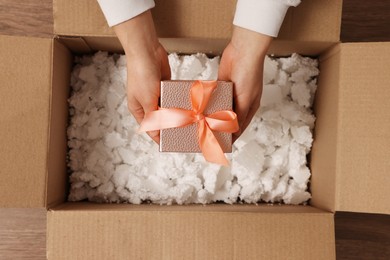 Photo of Woman putting Christmas gift box into parcel at wooden table, top view. Sending present by mail