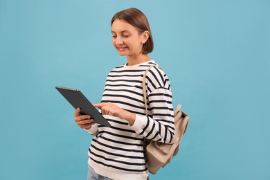 Young student with backpack and tablet on light blue background