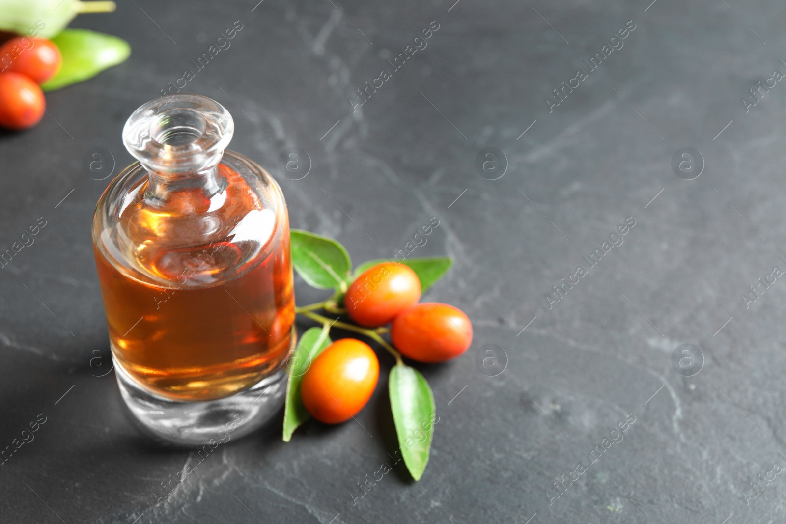 Photo of Glass bottle with jojoba oil and seeds on grey stone table. Space for text