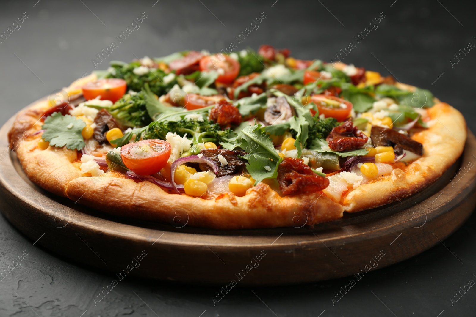 Photo of Delicious vegetarian pizza with cheese, mushrooms, vegetables and greens on black table, closeup