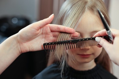 Photo of Professional hairdresser combing girl's hair in beauty salon, closeup