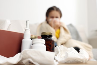 Photo of Girl blowing nose in tissue while on sofa in room, focus on medicines. Cold symptoms