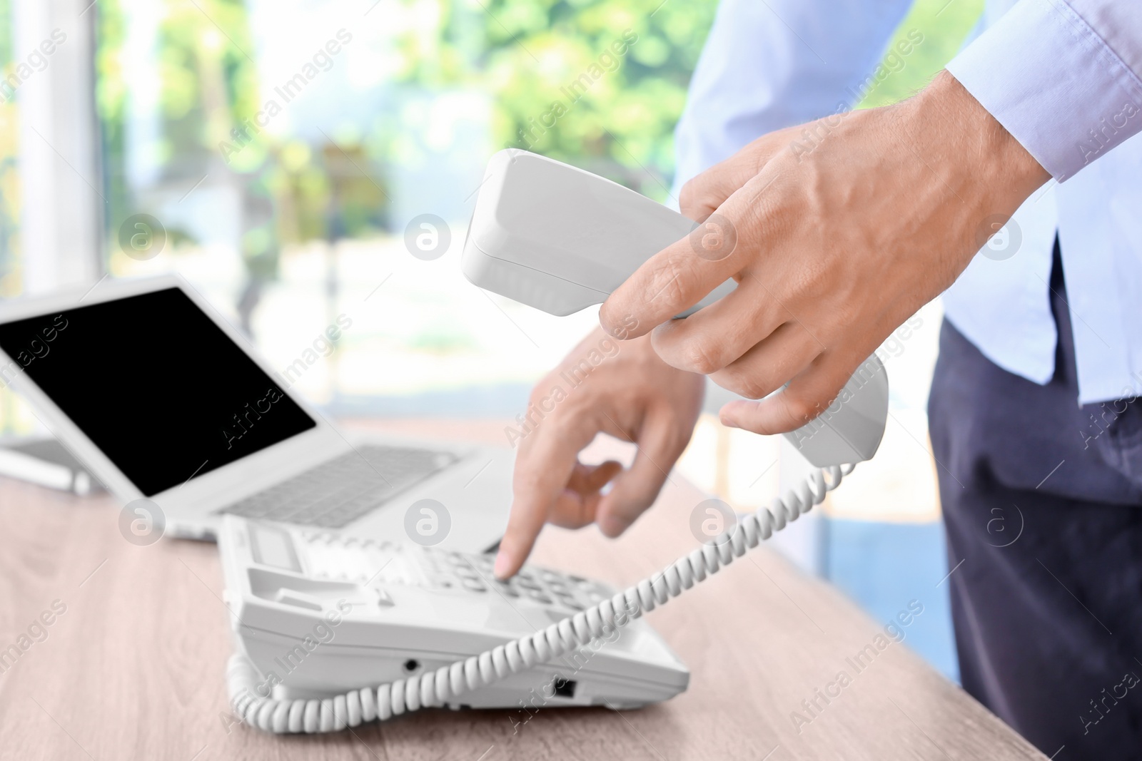 Photo of Man dialing number on telephone at workplace