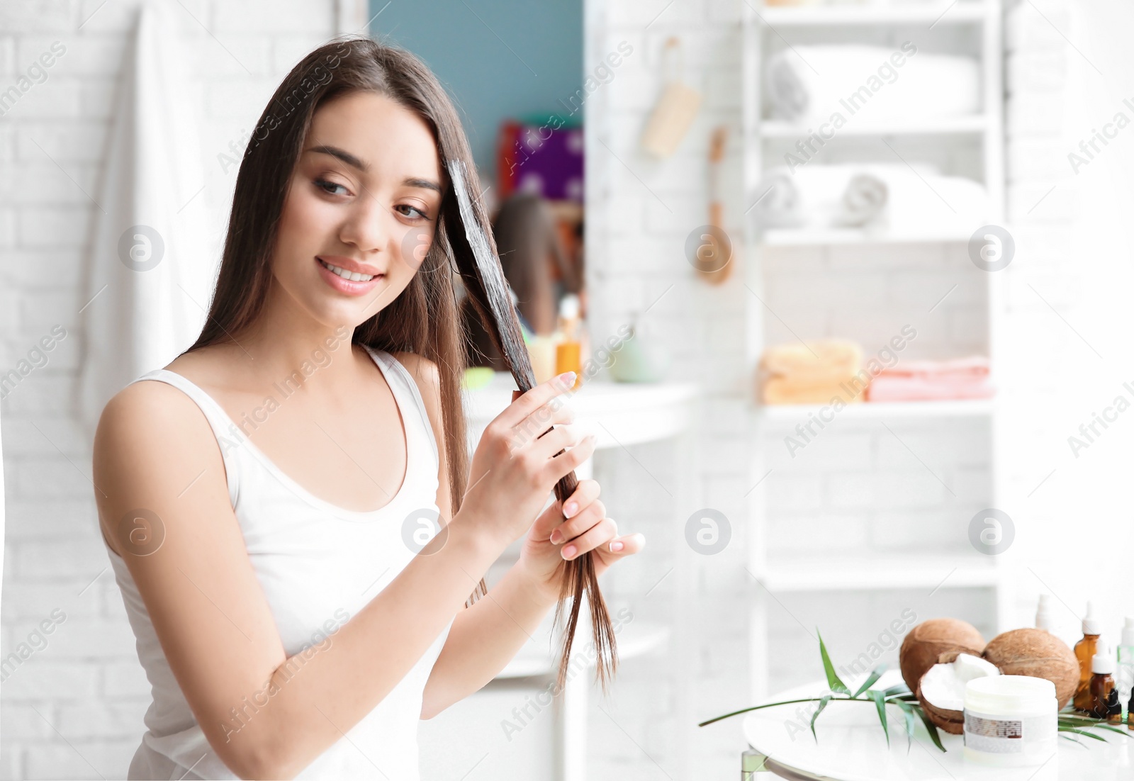 Photo of Young woman applying oil onto hair in bathroom