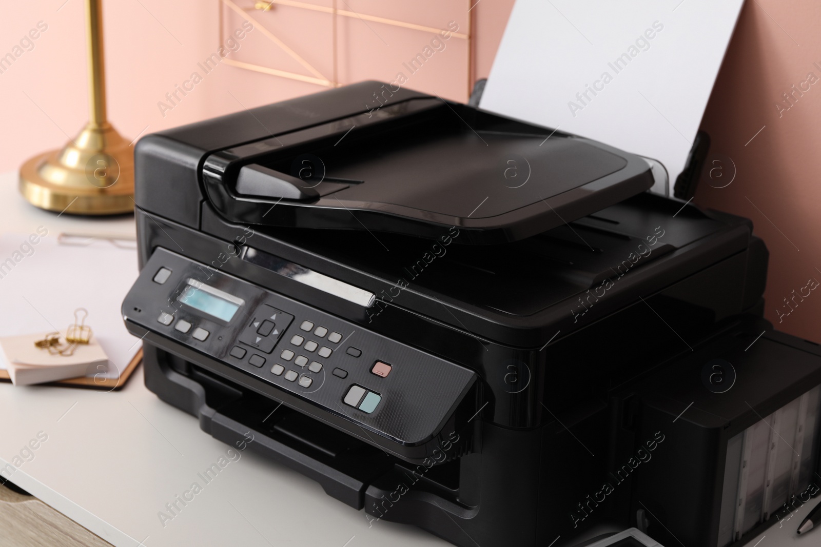 Photo of New modern printer with paper on white table at workplace