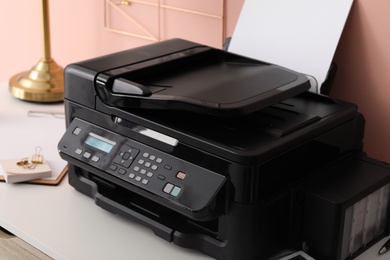 Photo of New modern printer with paper on white table at workplace