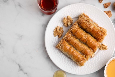 Photo of Eastern sweets. Pieces of tasty baklava, walnuts and tea on white marble table, flat lay. Space for text