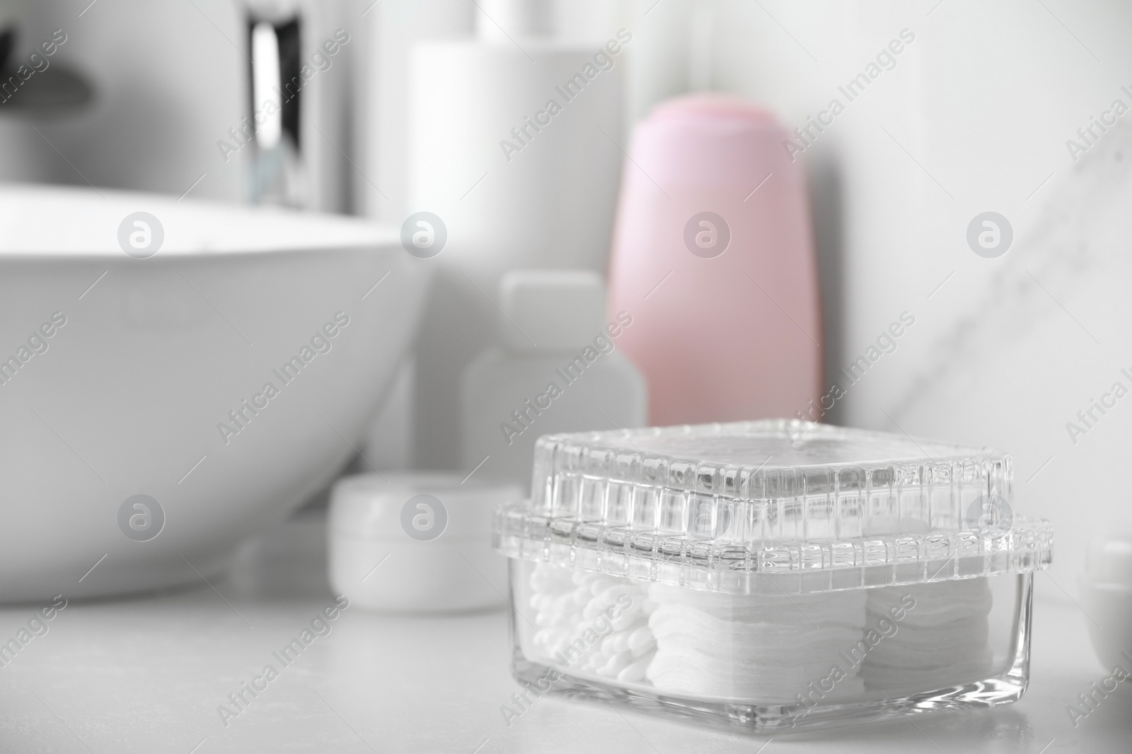 Photo of Container with cotton swabs and pads near cosmetic products on white countertop in bathroom. Space for text