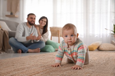 Photo of Happy parents watching their baby crawl on floor at home