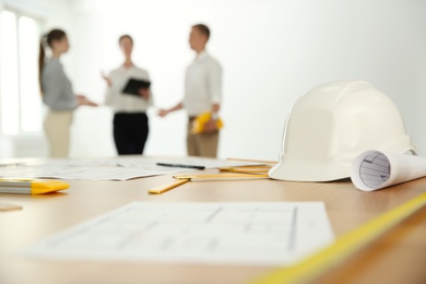 Photo of Colleagues in office, focus on table with construction drawings and tools