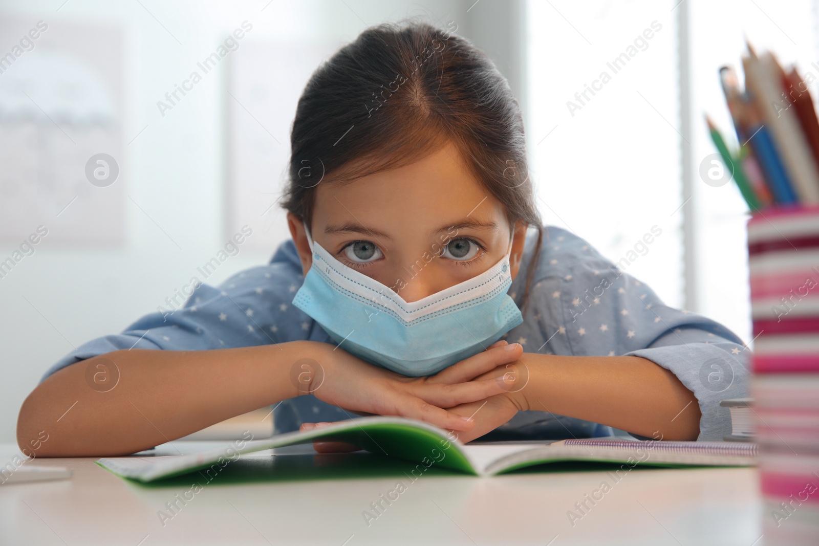Photo of Distance learning, online studying at home due to Covid-19 pandemic. Girl in protective mask doing homework in room