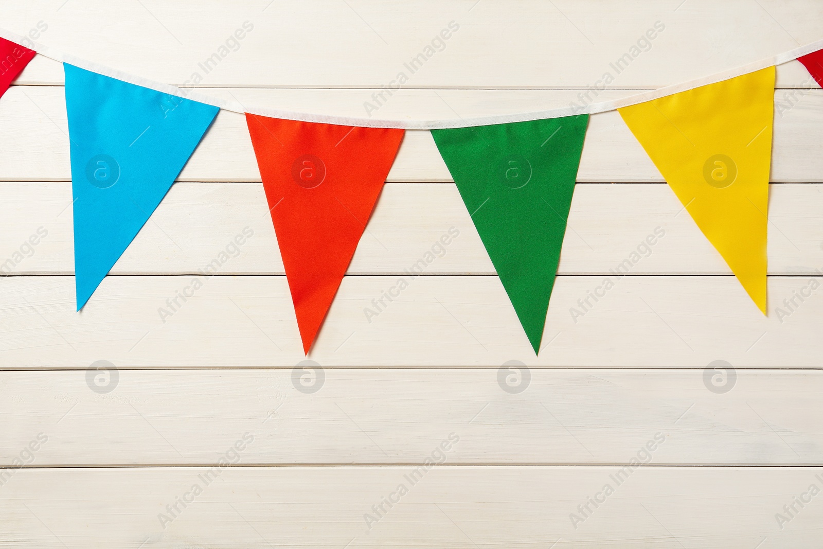Photo of Bunting with colorful triangular flags on white wooden background. Festive decor