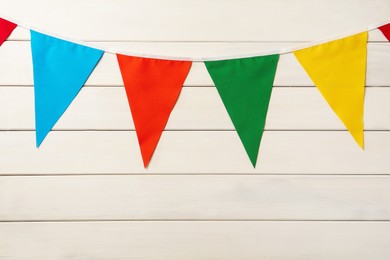 Bunting with colorful triangular flags on white wooden background. Festive decor