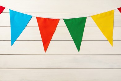 Photo of Bunting with colorful triangular flags on white wooden background. Festive decor