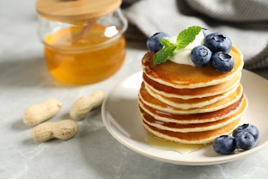 Photo of Plate of tasty pancakes with blueberries, sauce and mint on grey marble table