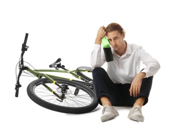 Depressed young man with bottle of wine near bicycle on white background