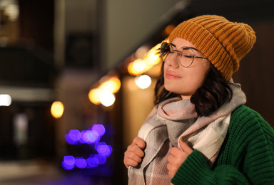 Photo of Young woman wearing warm sweater, hat and scarf  outdoors at night. Winter season