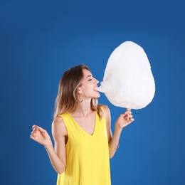 Photo of Happy young woman eating cotton candy on blue background