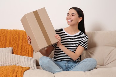 Photo of Happy young woman with parcel on sofa at home. Internet shopping