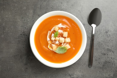 Photo of Bowl of tasty sweet potato soup and spoon on table, top view