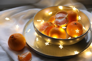 Photo of Fresh ripe tangerines and glowing fairy lights on white cloth