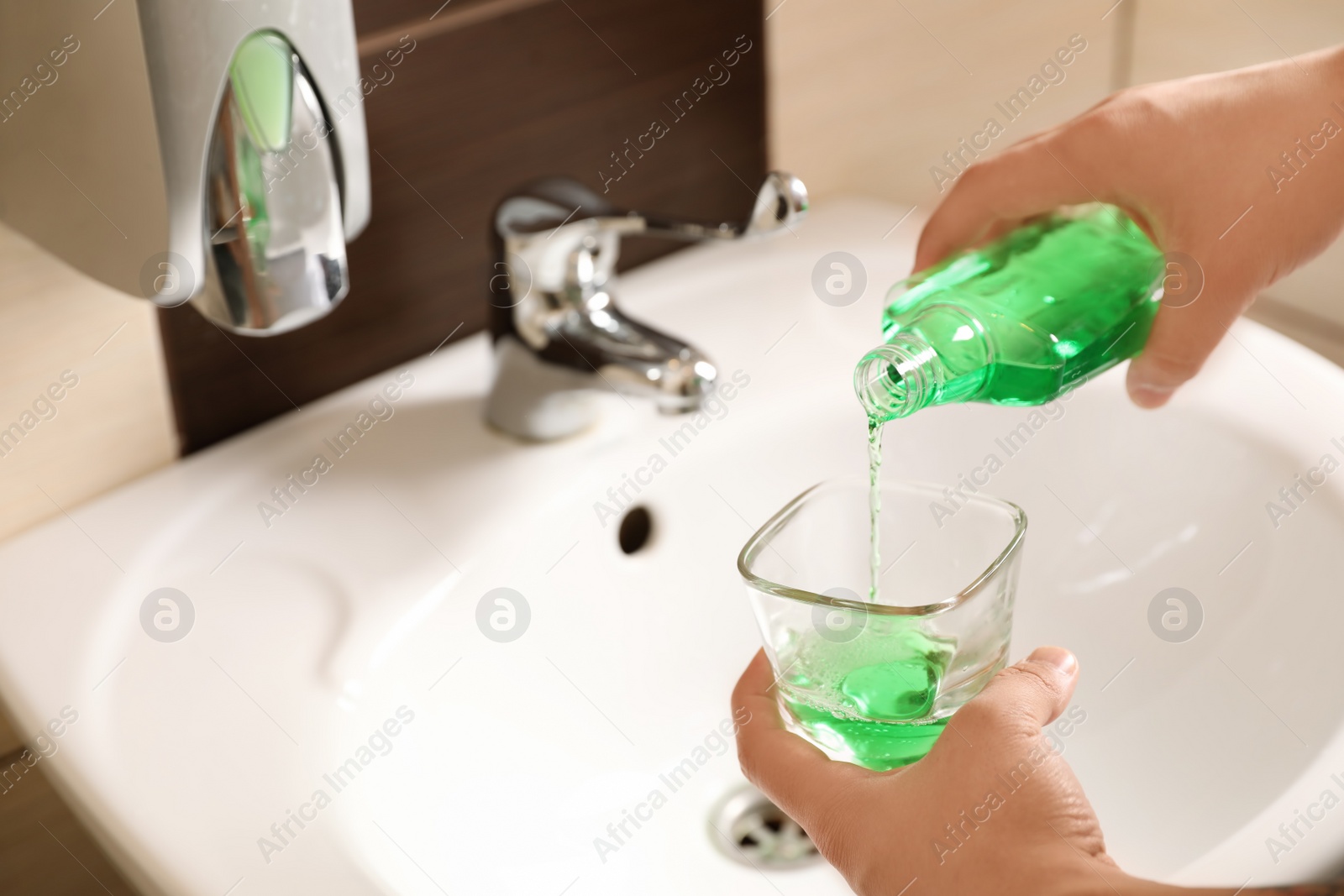 Photo of Man pouring mouthwash from bottle into glass in bathroom, closeup. Teeth care