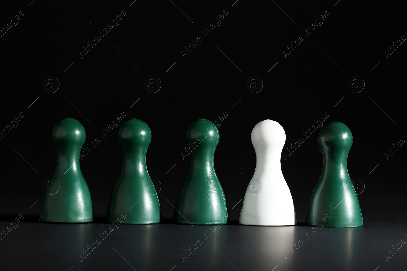 Photo of Choice concept. White pawn among green ones on black table, closeup