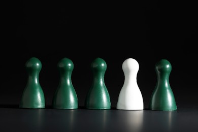 Photo of Choice concept. White pawn among green ones on black table, closeup