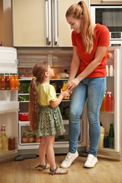 Young mother and daughter with juice near refrigerator at home