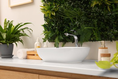 Green artificial plants, vessel sink and different personal care products in bathroom