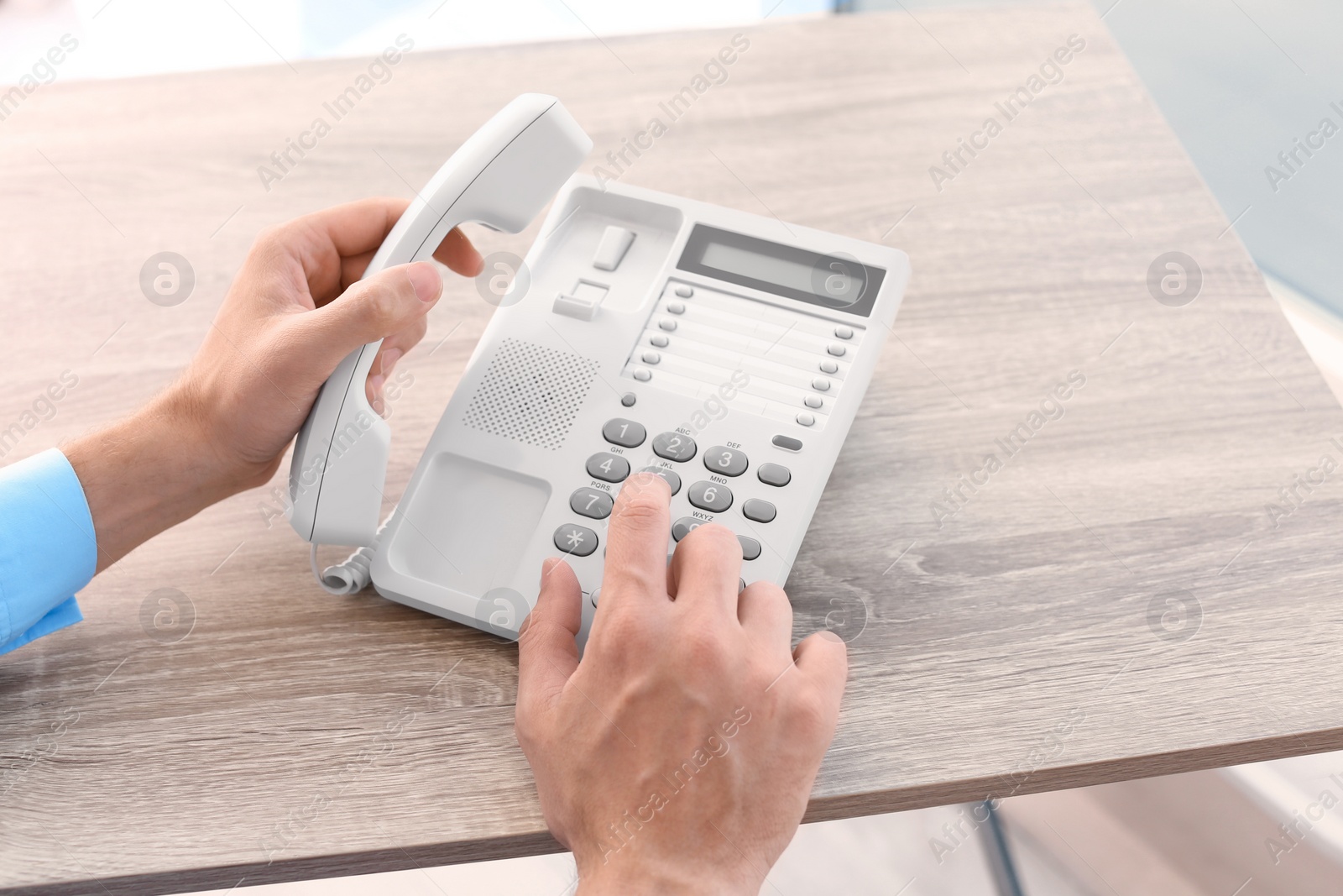 Photo of Man dialing number on telephone at table indoors